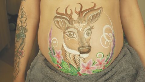 Pomalowany ciążowy brzuszek z wizerunkiem jelonka otoczonego kwiatami – symbol łagodności i nowego życia. Delikatny belly painting w pastelowych barwach, inspirowany naturą i macierzyństwem. - pełna rozdzielczość