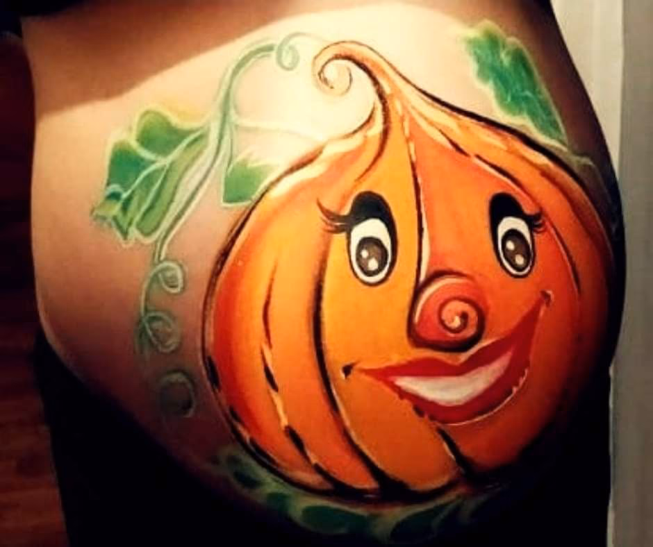 Kolorowy, pomalowany brzuch(brzuszek) ciążowy z motywem uśmiechniętej dyni otoczonej zielonymi liśćmi. Dynia jako symbol obfitości i radości, idealna na jesienne sesje ciążowe, baby shower lub tematyczne imprezy, takie jak Halloween. - w Lubinie, we Wrocławiu, w Brzegu, w Opolu, w Oławie, w Legnicy - zoptymalizowana wersja do szybkiego ładowania